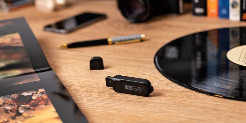 Zbliżenie na biurko z rozłożonym folderem, długopisem, telefonem i pendrive'em przypominającym zwykły nośnik USB.